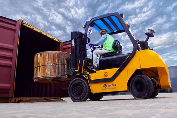 A man driving a forklift next to a shipping container.