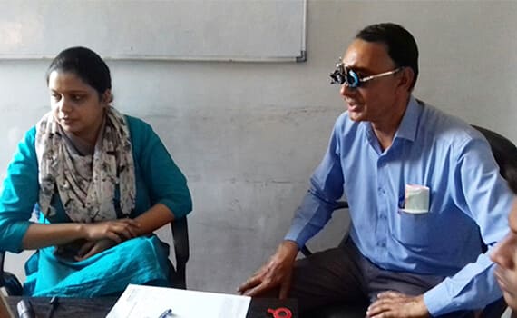 A man in blue shirt getting his eyes checked with a woman 