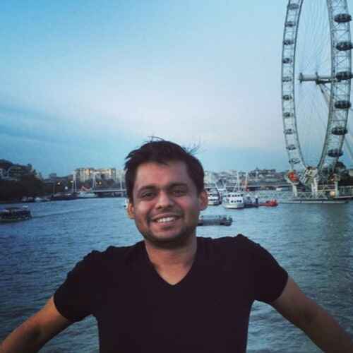 A person smiling in a tshirt with ferris wheel and river in background